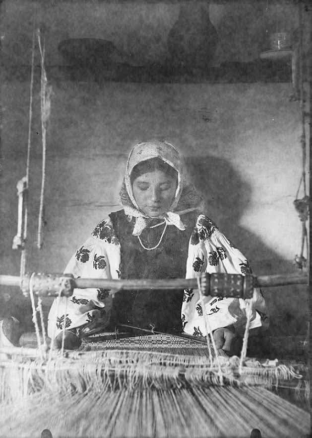 Femme au métier à tisser dans une maison traditionnelle, fils de chaîne visibles.