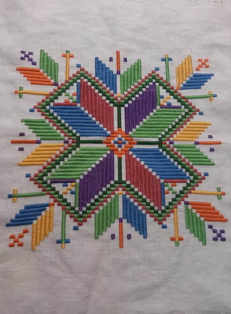 Détail de broderie géométrique multicolore sur lin blanc.