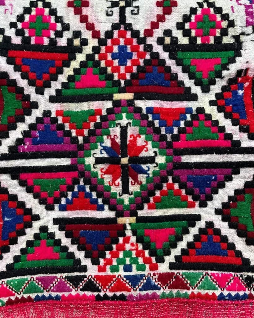 Broderie géométrique dense en rouge, bleu, vert et magenta sur fond clair.