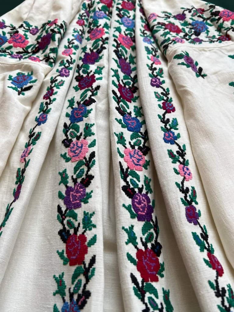 Bandes de broderie florale verticale sur lin crème, plis du tissu.