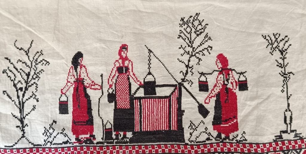 Broderie au point de croix : scène de village au puits avec trois femmes.